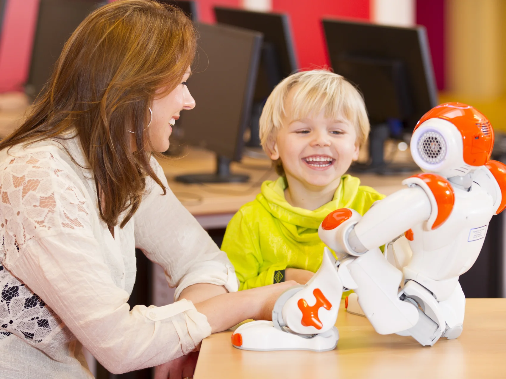 A woman and a young child play with a toy robot in a classroom